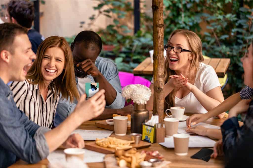 Best Conversation Cards for Couples 2 sincere laugh and showing picture on the smartphone at the casual meeting with best friends on the restaurant terrace